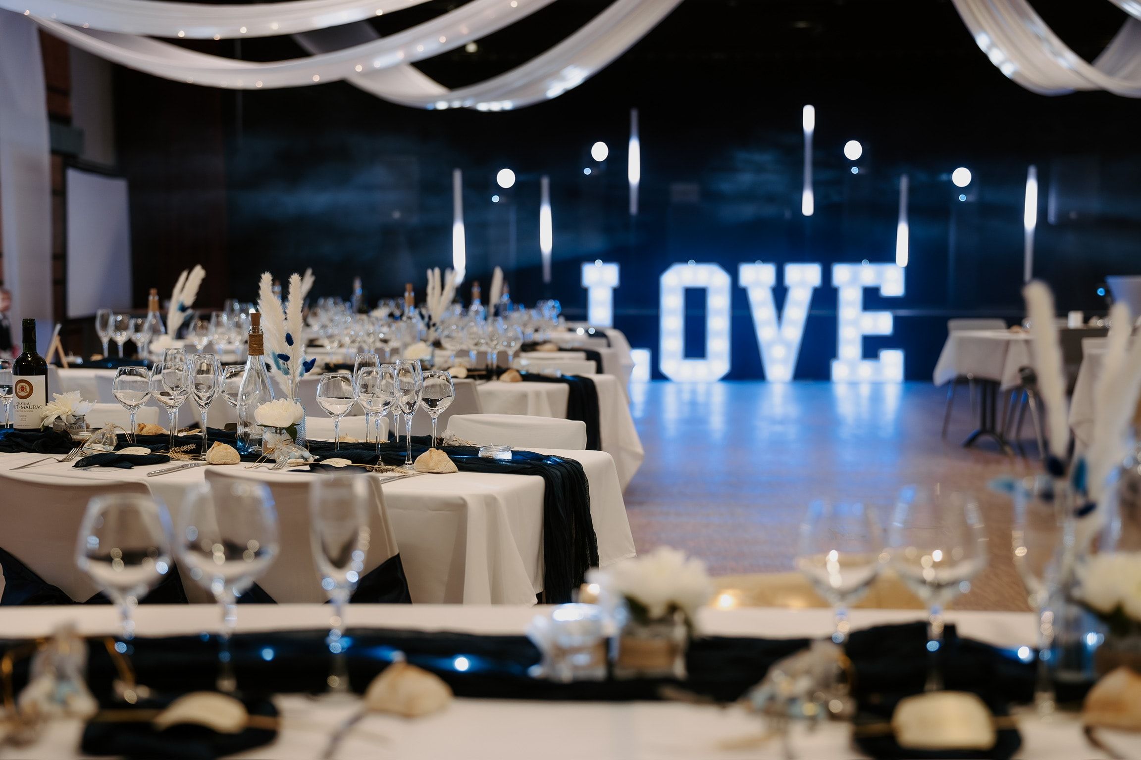 Les Lettres Lumineuses LOVE au fond d’une salle de réception dressée pour le dîner